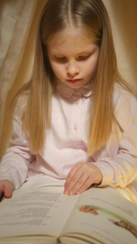 a little girl sitting on a bed reading a book, by Alice Mason, pexels, visual art, on a velvet table cloth, with long blond hair, 15081959 21121991 01012000 4k, wearing a light shirt