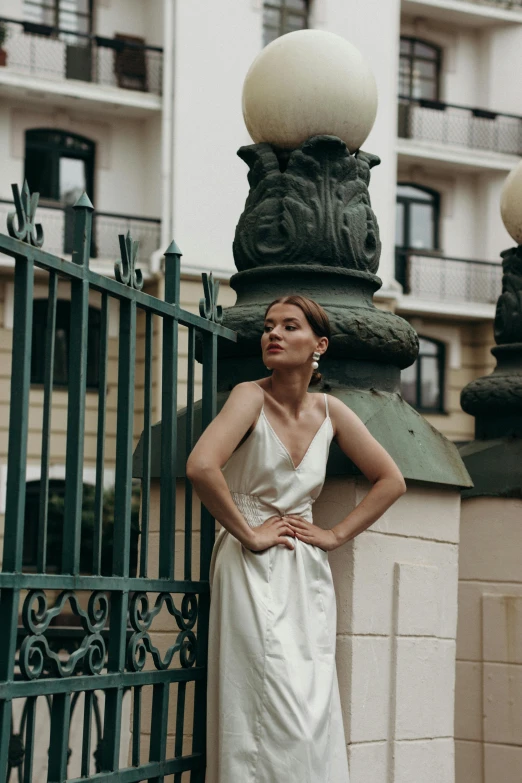 a woman in a white dress standing in front of a fence, inspired by Elsa Bleda, pexels contest winner, art nouveau, paris hotel style, girl with a pearl earringl, wearing a tanktop and skirt, formal wear