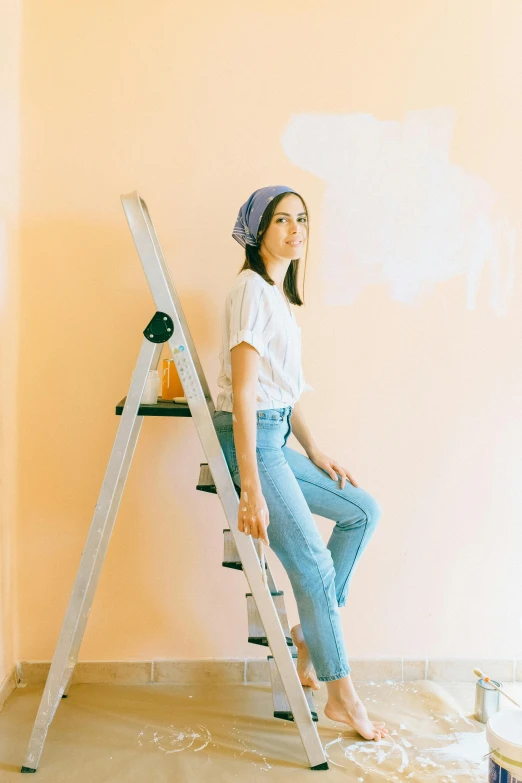 a woman sitting on a ladder in a room, trending on pexels, pastels, wearing jeans, pale orange colors, wall painting