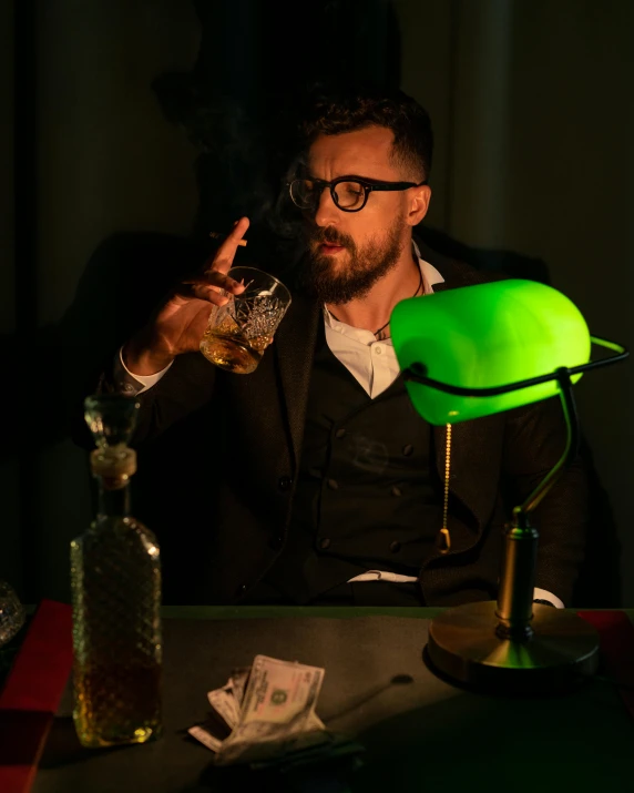 a man sitting at a table with a glass in his hand, an album cover, inspired by Joseph Wright of Derby, pexels contest winner, doug walker, bisexual lighting, ( ( theatrical ) ), green light