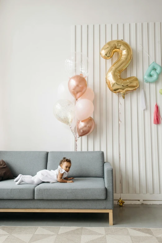 a little girl laying on a couch in a living room, party balloons, profile image, golden number, 2 years old