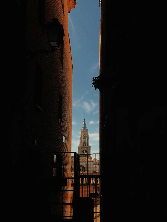 a view of a building with a clock tower in the background, a picture, unsplash contest winner, spanish ghibli alleyway, sun and shadow over a city, obscured underexposed view, tall spires