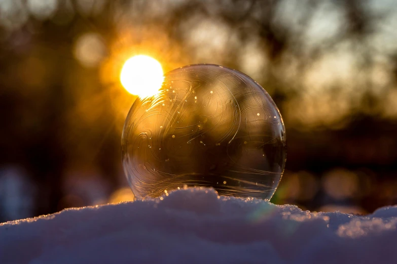 a glass ball sitting on top of snow covered ground, during a sunset