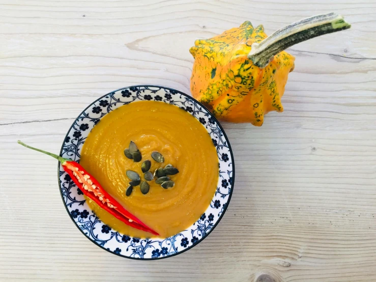 a bowl of soup sitting on top of a wooden table, inspired by Géza Dósa, unsplash, dau-al-set, pumpkin, square, vibrant colour, set against a white background