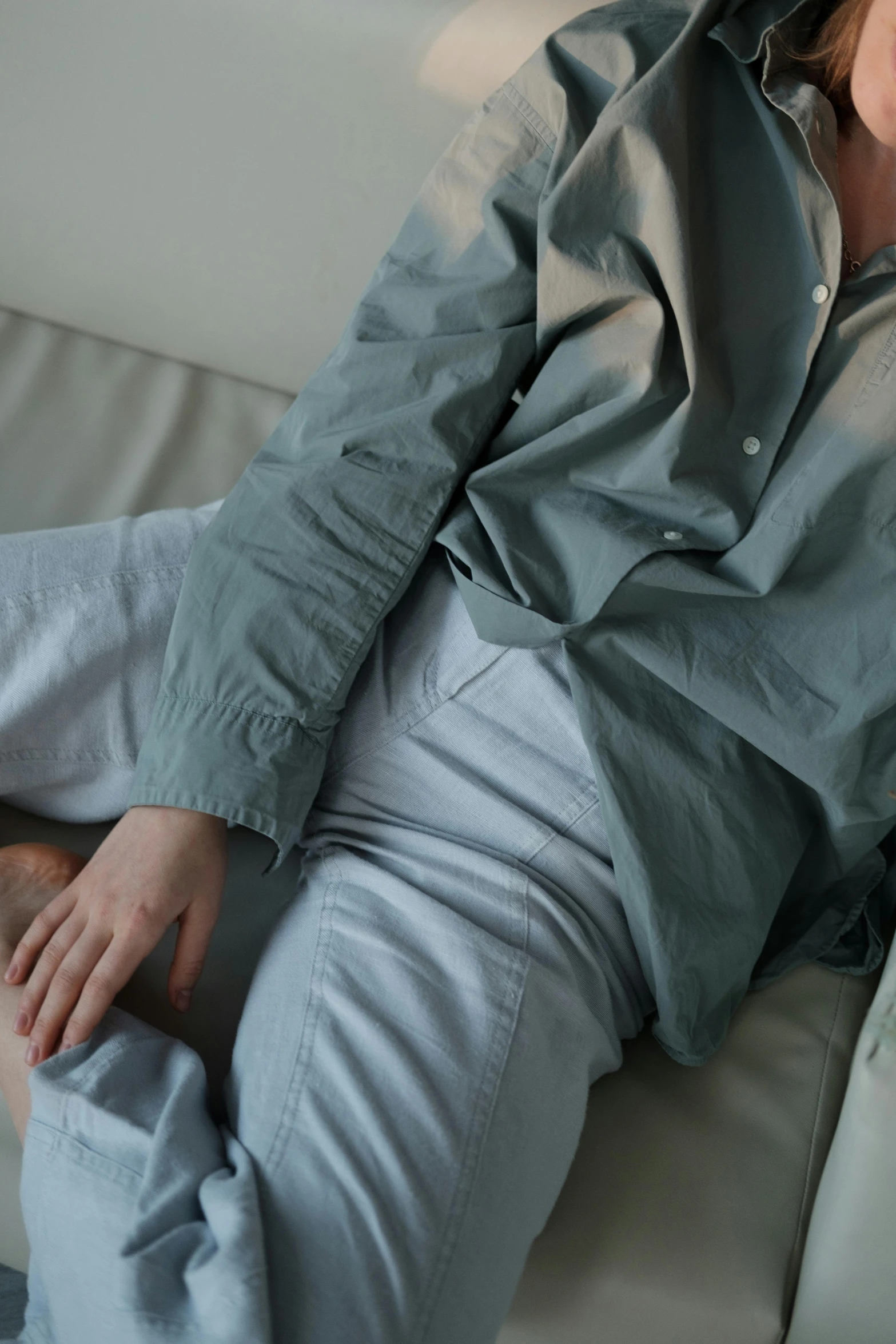 a woman laying on top of a white couch, by Yerkaland, wearing a light blue shirt, baggy pants, muted green, close up details
