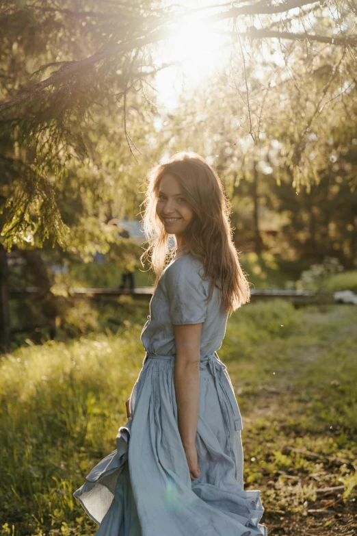 a woman in a blue dress standing in a field, profile image, smiling playfully, 2019 trending photo, morning sunlight