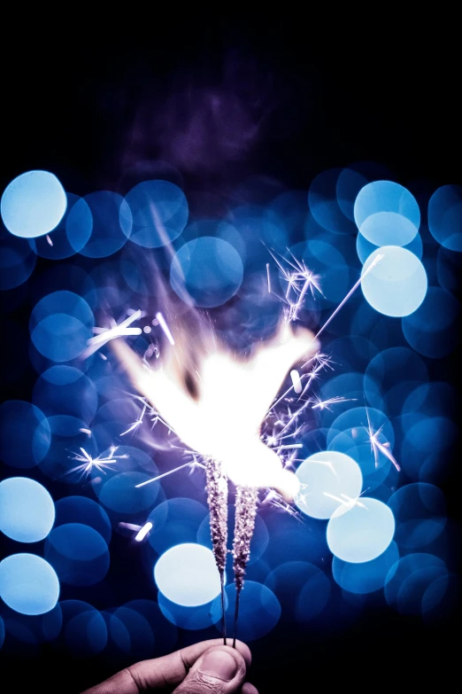 a person holding a sparkler in their hand, by Jan Rustem, emerging from blue fire, boke, celebration, close - up photograph