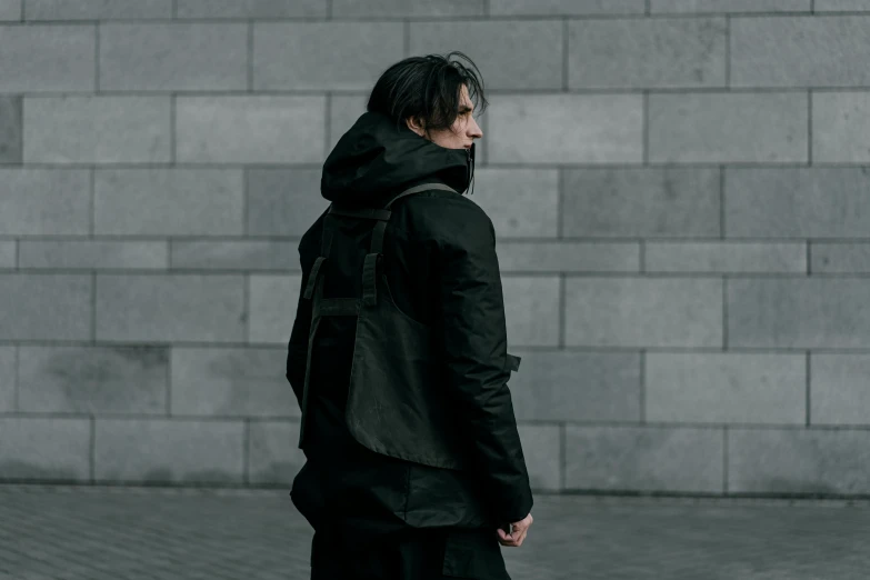a man standing in front of a brick wall, an album cover, inspired by Kanō Hōgai, unsplash, black tactical gear, trench coat with many pockets, victoria siemer, architect