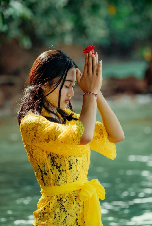 a woman in a yellow dress standing next to a body of water, inspired by Lü Ji, pexels contest winner, prayer hands, vietnamese woman, wearing a flower headpiece, teenage girl