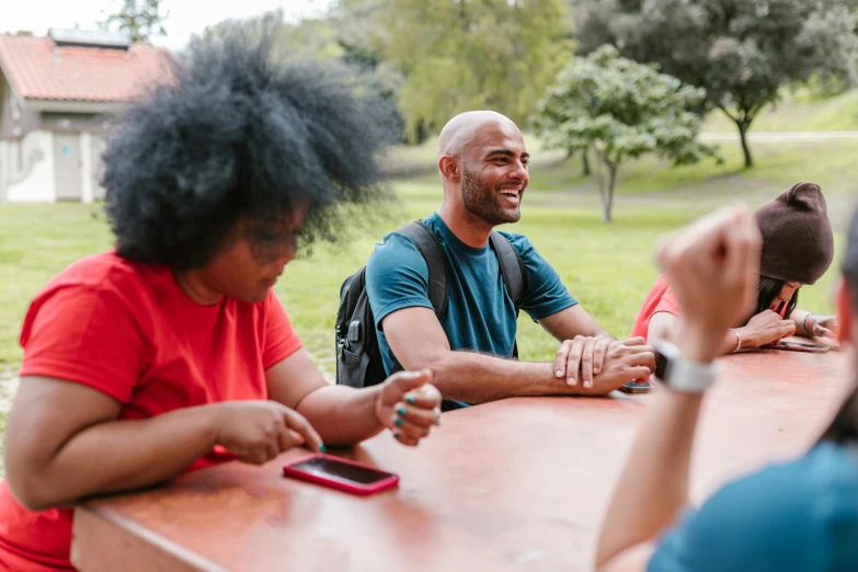 a group of people sitting around a wooden table, pexels contest winner, happening, at a park, black man with afro hair, te pae, smiling at each other