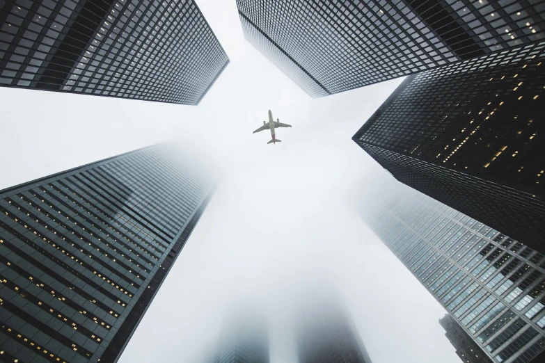 a plane flying over a group of tall buildings, by Adam Rex, pexels contest winner, foggy day, national geographic photo award, toronto city, looking up into the sky