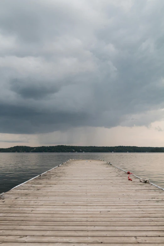 a dock next to a body of water under a cloudy sky, thunderstorm outside, looking towards camera, turbulent lake, color photograph