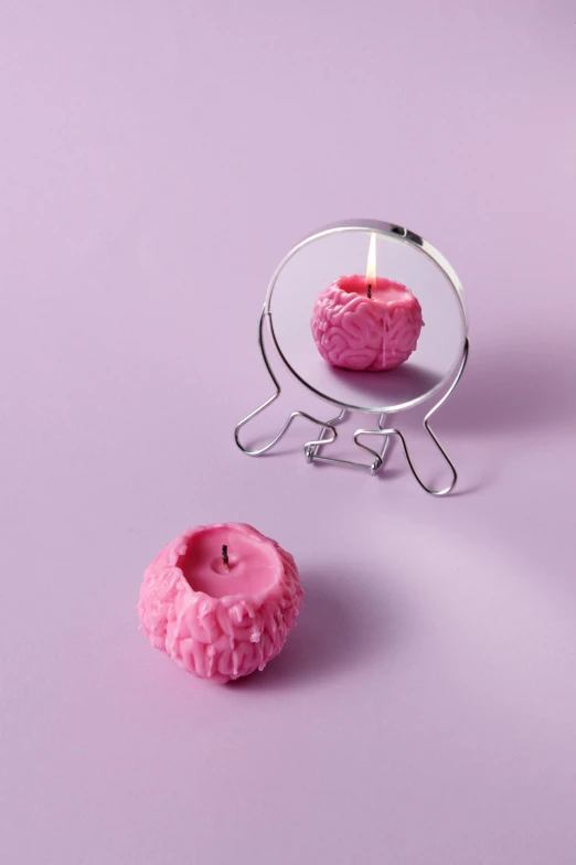 a pink candle sitting on top of a table next to a mirror, a surrealist sculpture, inspired by Marina Abramović, miniature human brain, detailed product image, candy apple, dwell