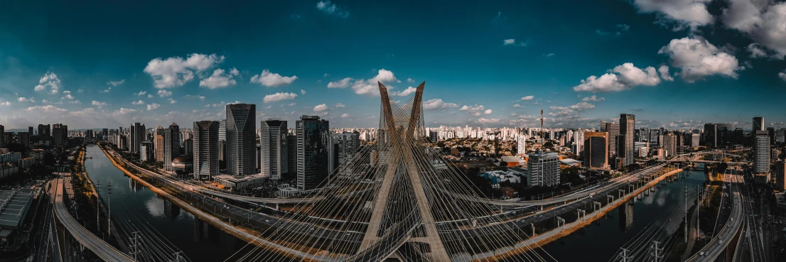 a view of a city from the top of a bridge, by Joze Ciuha, pexels contest winner, oscar niemeyer, skybridge towers, blue sky, view from helicopter