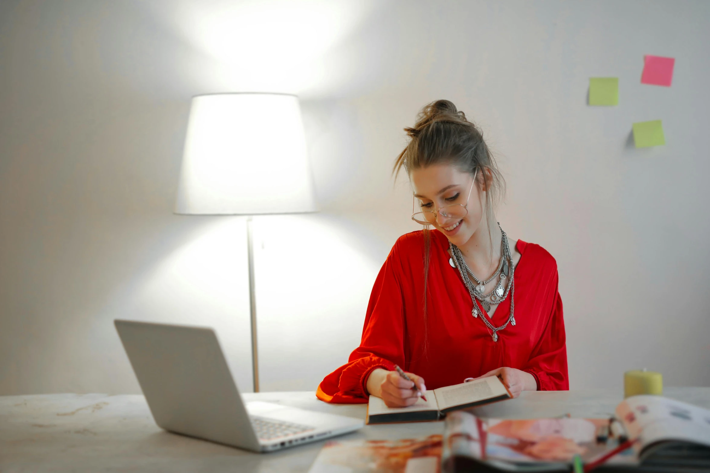 a woman sitting at a table in front of a laptop, trending on pexels, academic art, wearing red attire, orange lamp, red ballpoint pen, emerging from her lamp