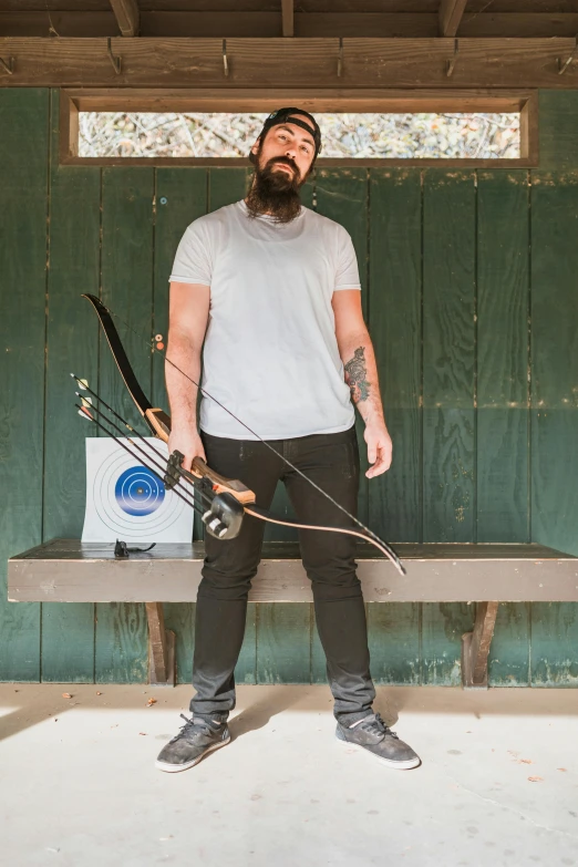 a man with a beard holding a bow and arrow, aaron sims, casually dressed, photograph