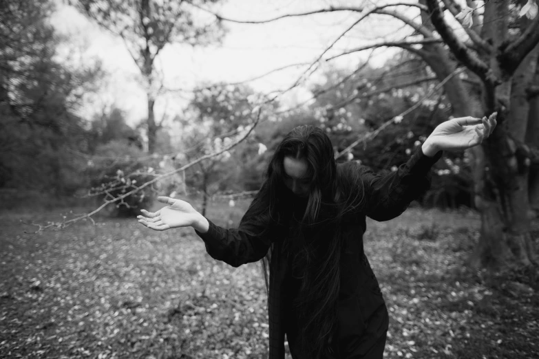 a black and white photo of a person in the woods, unsplash, conceptual art, shrugging arms, dressed in dark garment, branches, crying and reaching with her arm