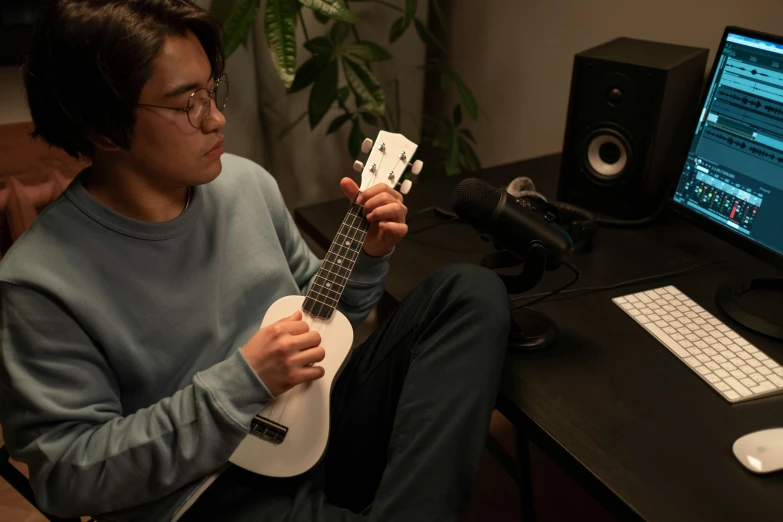 a man sitting in front of a computer playing a ukuleta, inspired by Reuben Tam, unsplash, teenage engineering moad, japanese collection product, promotional photo, from 8 k matte