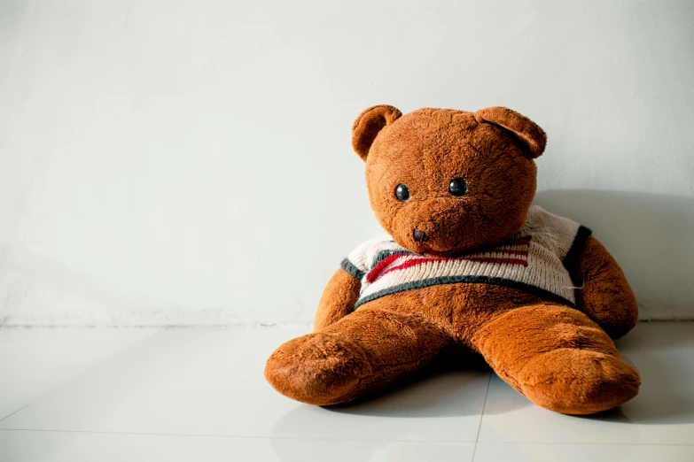 a brown teddy bear sitting on a white floor