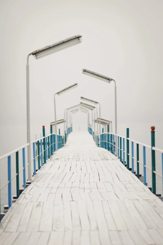 a bridge over a body of water on a foggy day, a minimalist painting, inspired by Ryoji Ikeda, unsplash contest winner, ukraine. photography, boardwalk, covered with snow, seaside