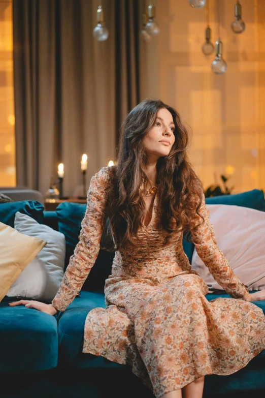 a woman sitting on a couch in a living room, pexels contest winner, arabesque, long brown wavy hair, wearing a long dress, style of julia razumova, candlelit