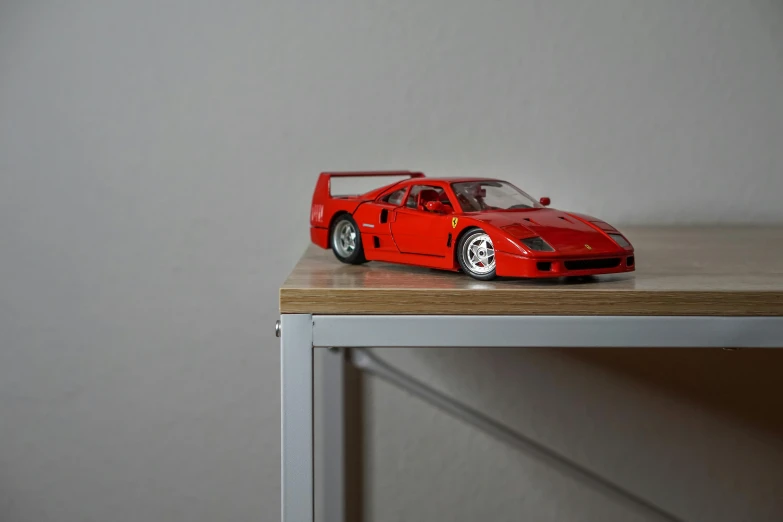 a red toy car sitting on top of a wooden table, inspired by Bernardo Cavallino, unsplash, photorealism, ferrari f 4 0, standing on a shelf, high resolution print :1 red, in my bedroom