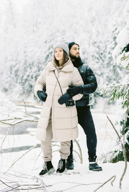 a man and woman standing next to each other in the snow, inspired by Salomon van Abbé, trending on pexels, long coat, foliage clothing, thumbnail, puffer jacket