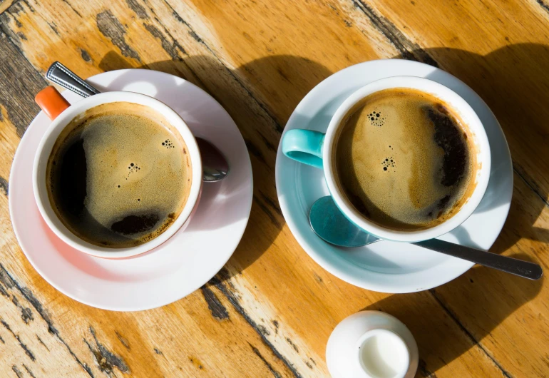 two cups of coffee sitting on top of a wooden table, trending on unsplash, jen atkin, brown and cyan color scheme, multiple stories, in the sun