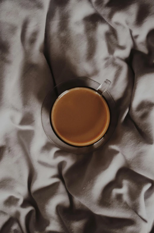 a cup of coffee sitting on top of a bed, on a velvet tablecloth, light tan, dark hues, - 9