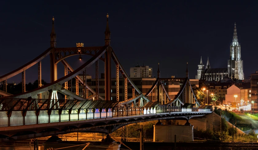 a bridge over a river with a city in the background, by Adam Marczyński, pexels contest winner, asymmetrical spires, night time footage, chesterfield, slide show