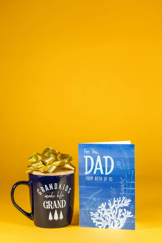 a cup of coffee and a card on a yellow background, by Gwen Barnard, dada, dad, blue and gold color scheme, hero shot, thumbnail