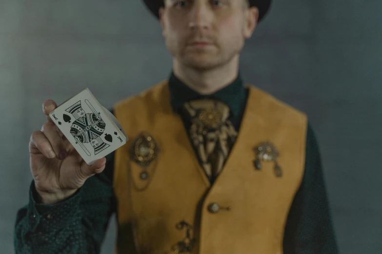 a man in a yellow vest holding a playing card, a portrait, pexels contest winner, wearing steampunk top hat, structure : kyle lambert, holding a 🛡 and an 🪓, symmetrical shot