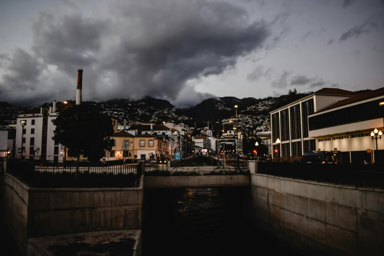 a river running through a city under a cloudy sky, by Alejandro Obregón, pexels contest winner, modernism, dark neighborhood, wellington, in the evening, location ( favela _ wall )