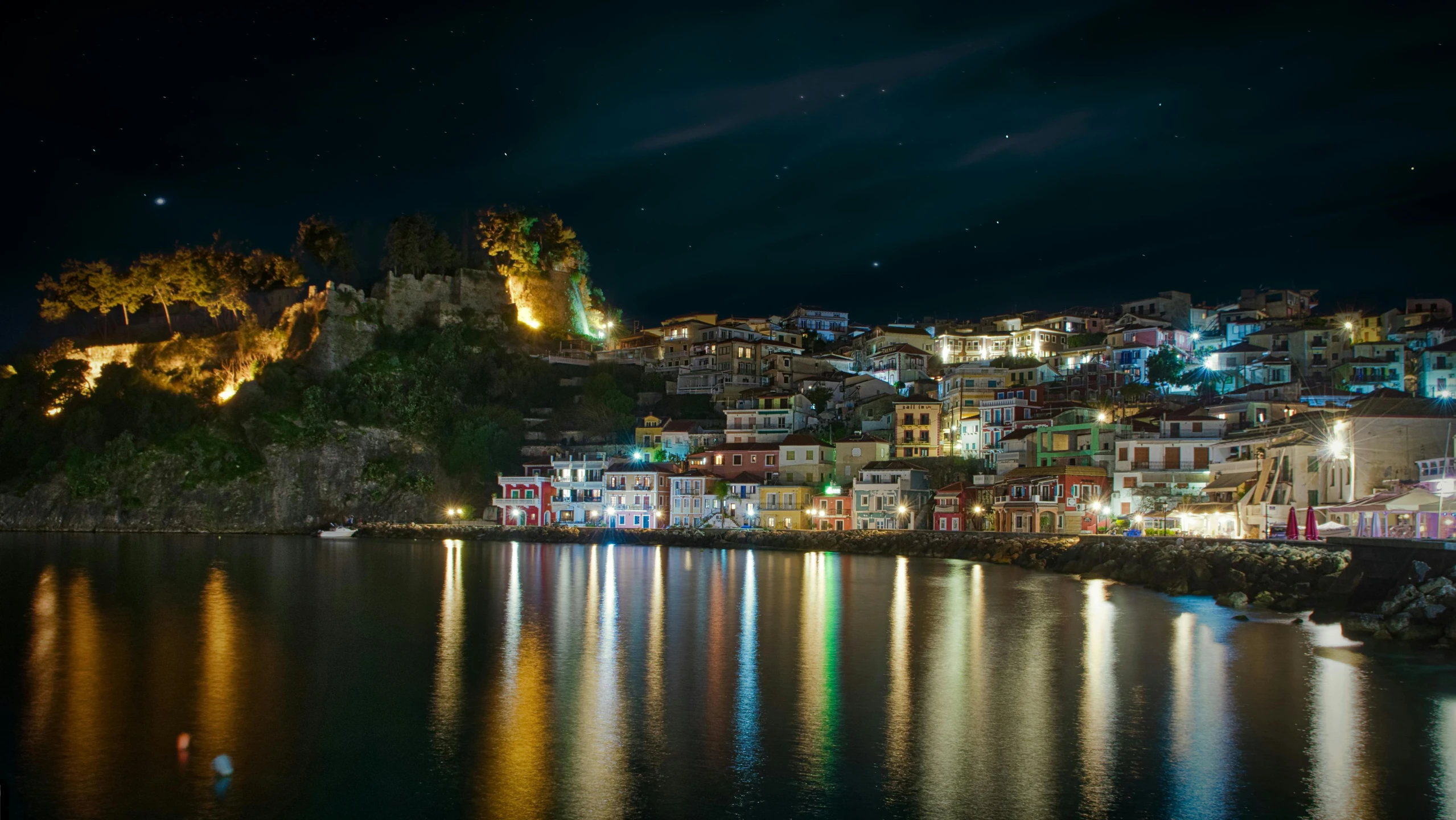 a city lit up at night next to a body of water, by Michalis Oikonomou, pexels contest winner, the village on the cliff, square, coloured, reflecting