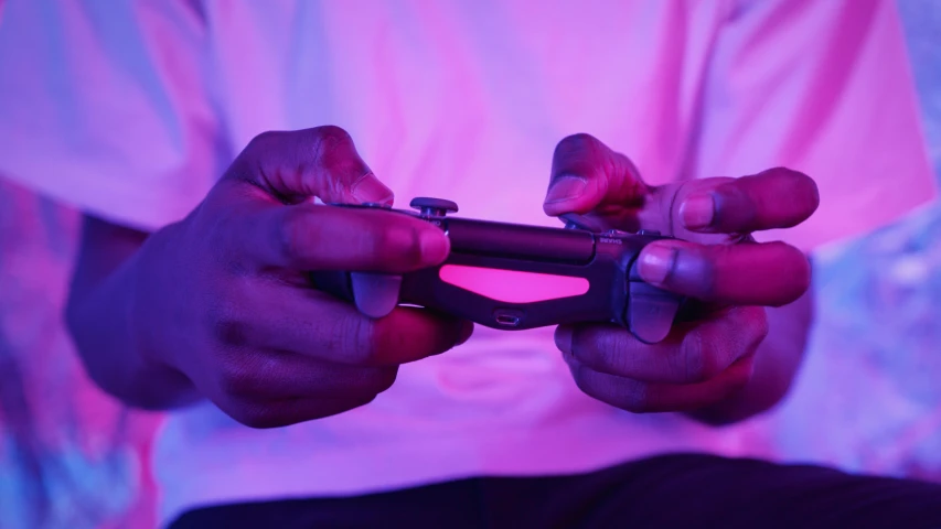 a person holding a video game controller in their hands, by Matija Jama, pexels, soft neon purple lighting, ( ( dark skin ) ), pink and purple, chilling