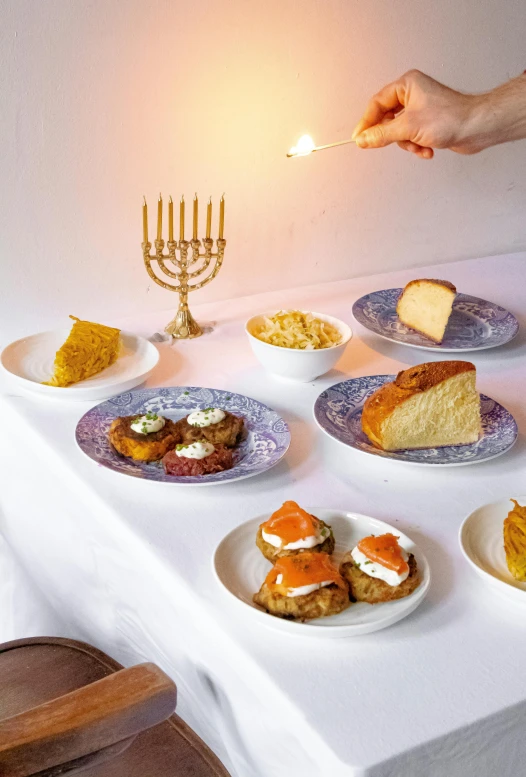 a white table topped with plates of food, holy lights, bread, julia sarda, holding a candle holder