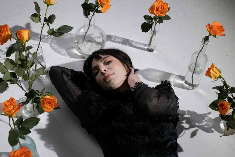 a woman laying on the ground surrounded by flowers, an album cover, trending on pexels, charli xcx, on a white table, actors, androgynous person