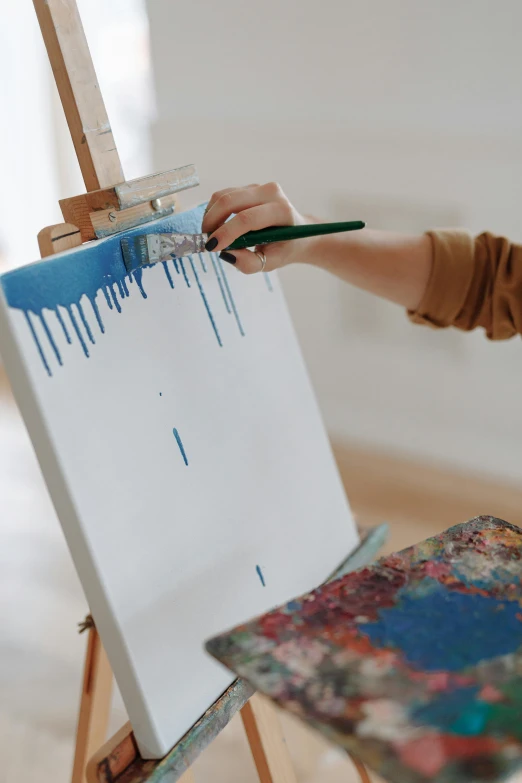 a woman is painting a picture on an easel, pexels contest winner, blue drips, on a white table, on canvas, trending on artstaion