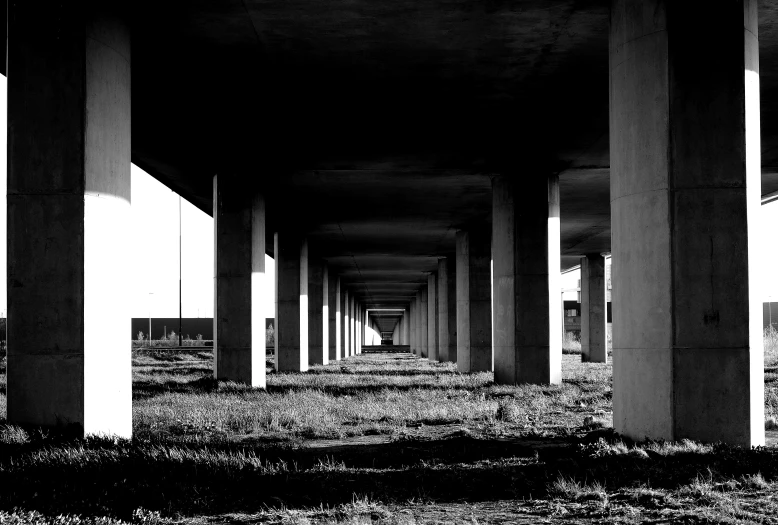 a black and white photo of an underpass, a black and white photo, inspired by Thomas Struth, unsplash, brutalism, concrete pillars, ground view, afar, ilford delta 3200