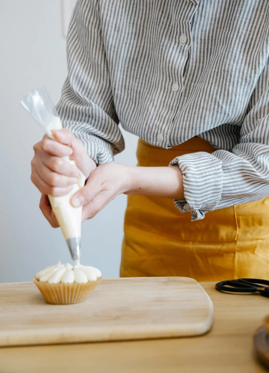 a woman is putting icing on a cupcake, inspired by Sarah Lucas, pexels, full product shot, tall, transparent, handheld