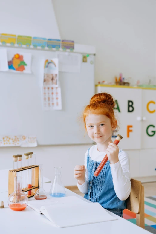 a little girl sitting at a table in a classroom, pexels contest winner, one is a redhead, whiteboards, kids toys, blippi