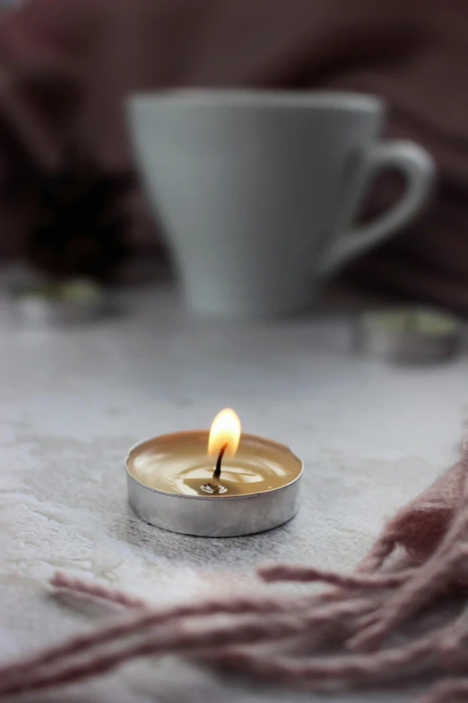 a candle sitting on top of a table next to a cup, a picture, silver and muted colors, soft light - n 9, miniature product photo, low detail