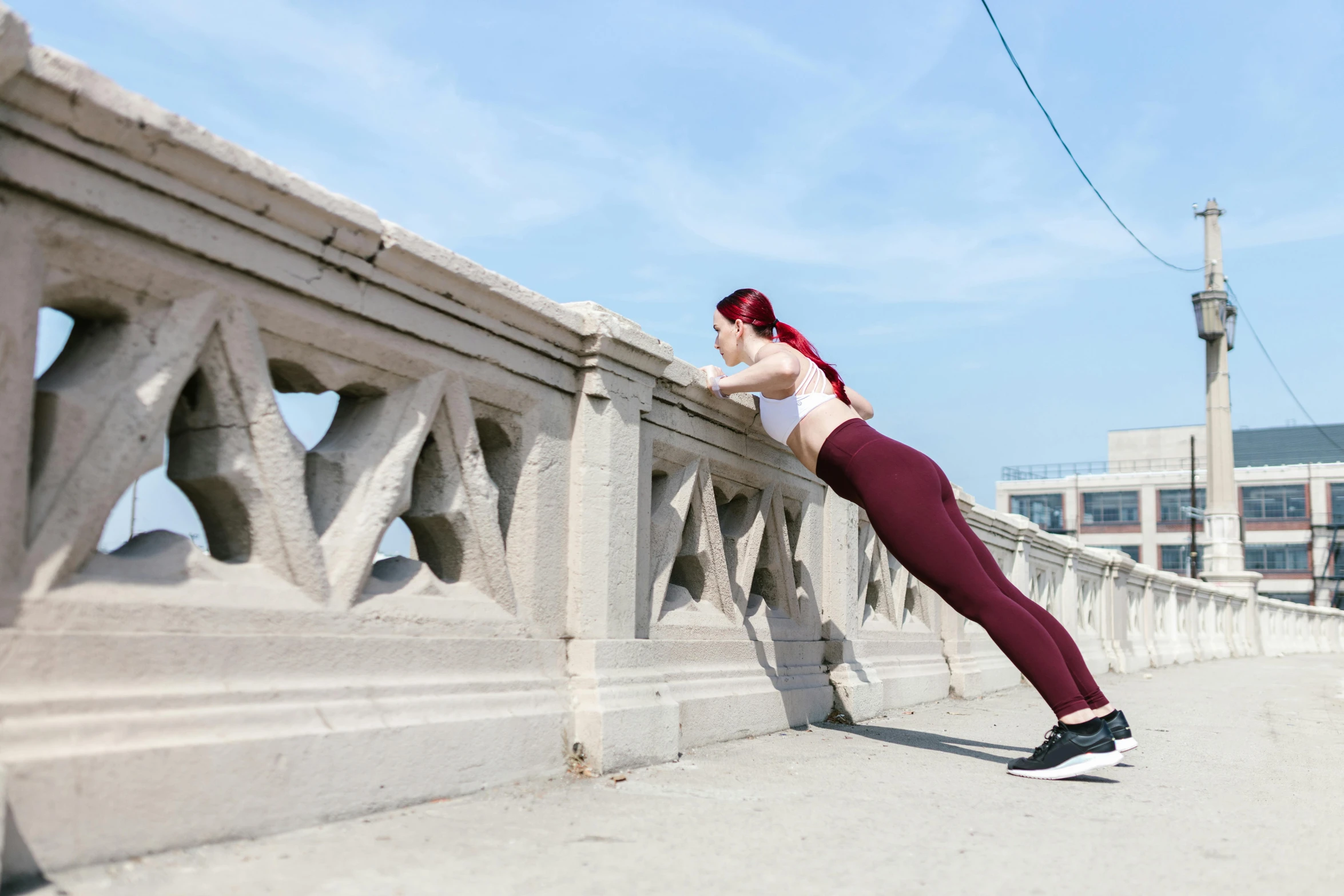 a woman stretching her legs on a bridge, trending on pexels, arabesque, maroon and white, exposed midriff, background image, parapets