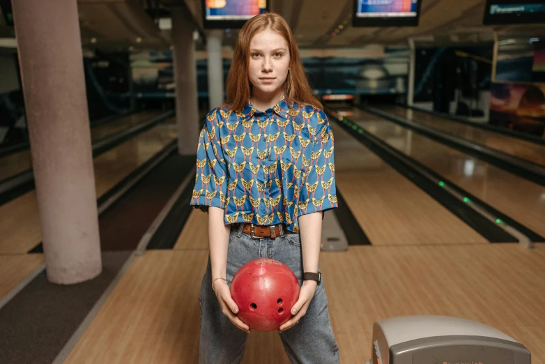 a woman holding a bowling ball in a bowling alley, by Julia Pishtar, wearing a shirt and a jean, sadie sink, blue - print, posed