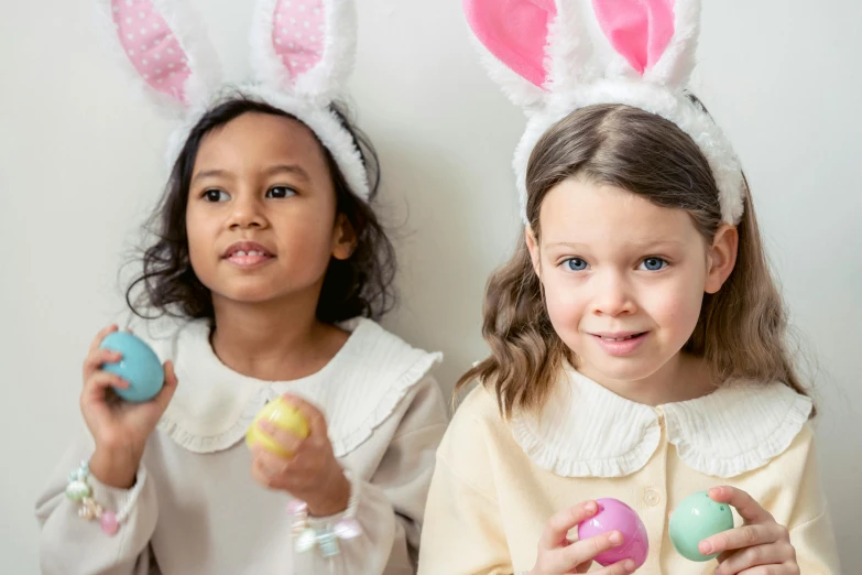 two girls in bunny ears holding easter eggs, by Ellen Gallagher, pexels contest winner, professionally retouched, looking towards camera, varying ethnicities, lena oxton