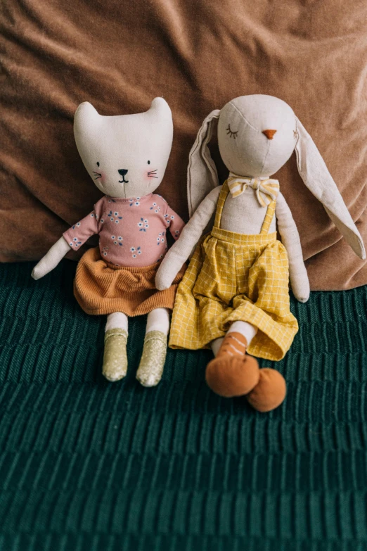 two stuffed animals sitting next to each other on a bed, by Emma Andijewska, holding a rabbit, yellow clothes, on a wooden table, thumbnail