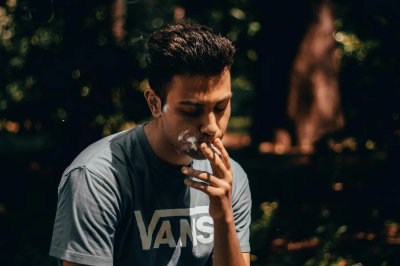 a man smokes a cigarette in the park, pexels contest winner, avatar image, wearing a shirt, he is about 20 years old | short, profile image