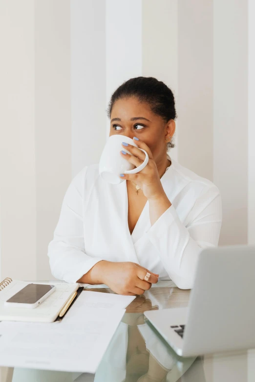 a woman sitting at a desk with a laptop and a cup of coffee, by Dulah Marie Evans, wearing a white blouse, pondering, drinking a cup of coffee, profile image