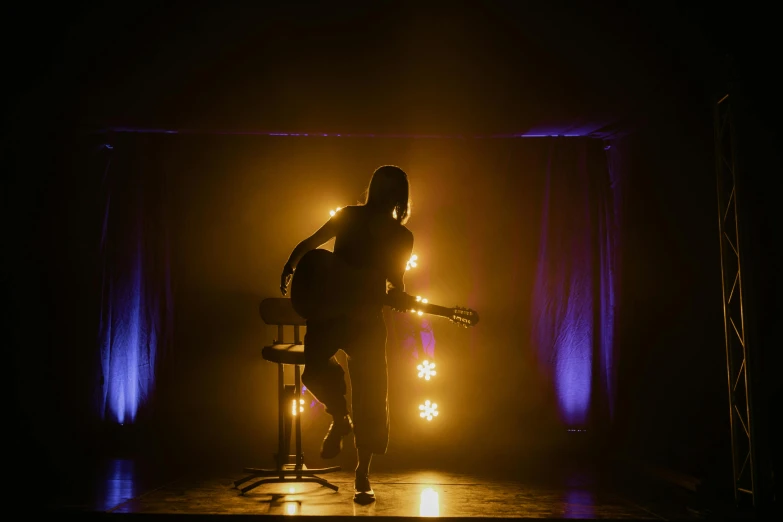 a person standing on a stage with a guitar, film lighting, hammershøi, back facing, ( ( theatrical ) )