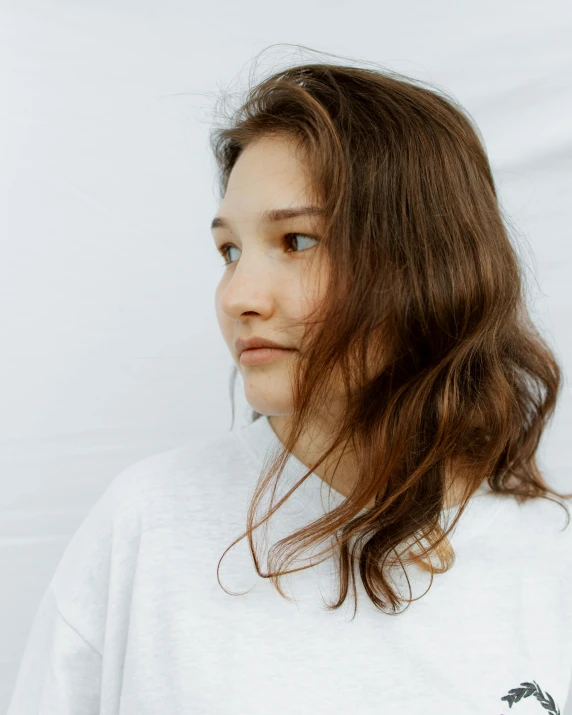 a woman with long brown hair wearing a white shirt, trending on unsplash, non binary model, looking partly to the left, clumps of hair, human staring blankly ahead